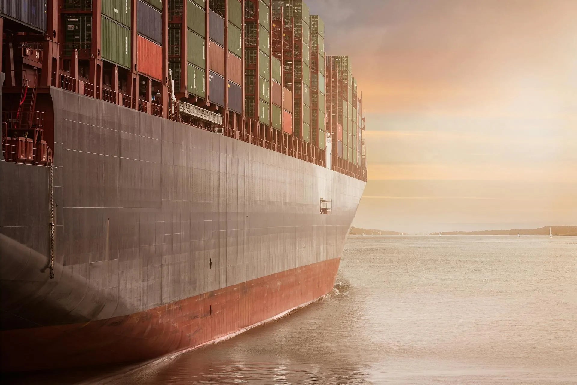 Bow of a large container vessel underway on open water at sunset.