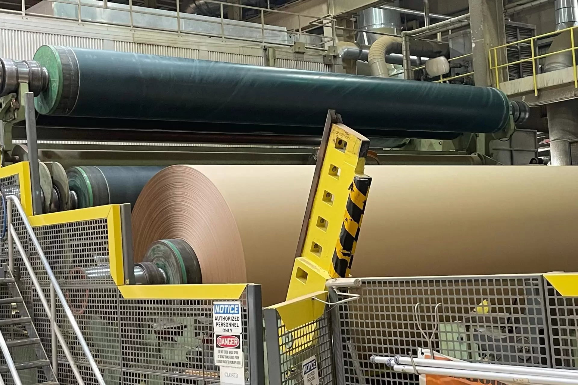 Paper mill machinery with high-speed rollers and continuous web of paper running through.